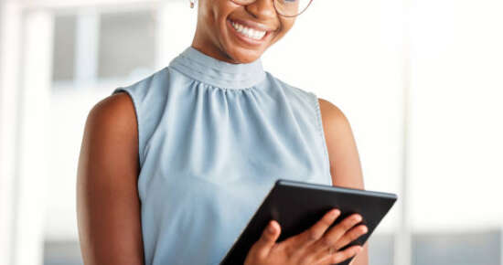 Young cheerful african american businesswoman working on a digital tablet alone at work. Happy black woman smiling while using social media on a digital tablet. Businessperson checking an email on a digital tablet